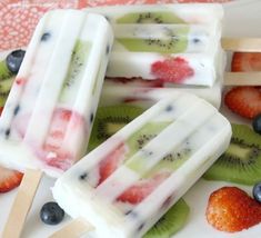 three popsicles with kiwis and blueberries on them sitting on a plate