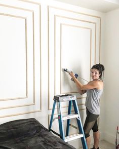 a woman is painting the wall in her bedroom with a ladder and paint rollers