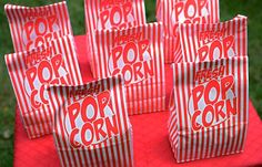 red and white striped popcorn bags sitting on top of a table with green grass in the background