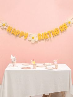 a happy birthday banner hanging over a table with plates and cups on it in front of a pink wall