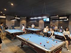 a group of people playing pool in a room with many tables and balls on it