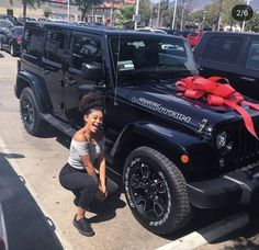 a woman kneeling next to a black jeep with a red bow on it's hood