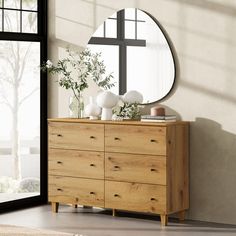 a wooden dresser with a mirror and vases on it in front of a window