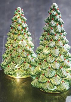 two green christmas trees sitting on top of a table next to each other with red berries