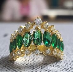 a close up of a ring with green stones and diamonds on the inside of it