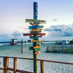 a sign post on the beach with many signs pointing to different locations and places around it