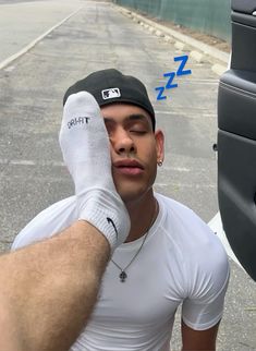 a man in white shirt and black hat holding his hand up to his face next to a parking meter