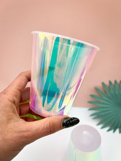 a hand holding a cup that has been painted with multicolored paint on it