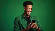 a man smiling and looking at his cell phone while standing in front of a green background