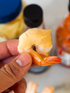 a person holding up a piece of food with shrimp on it's tip and sauce in the background