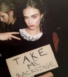 a young woman holding a sign that says take me back stage and pointing at it