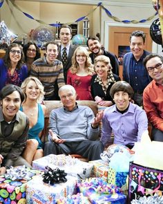 a group of people sitting around each other with presents on the floor and balloons in the background