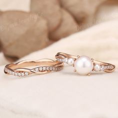 two gold rings with pearls and diamonds on them sitting on a white surface next to rocks