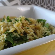 a white bowl filled with pasta and spinach on top of a yellow table cloth