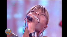 a woman singing into a microphone while holding her hands up to her face with both hands