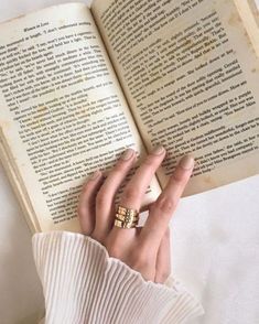 a woman is holding an open book in her left hand and wearing two gold rings