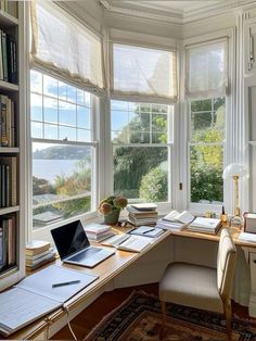 a desk with a laptop on it in front of two windows and a book shelf