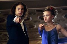 a man and woman dressed in formal wear pointing at something on the wall behind them