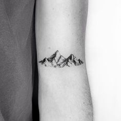 a black and white photo of a mountain tattoo on the left arm, with snow capped mountains in the background