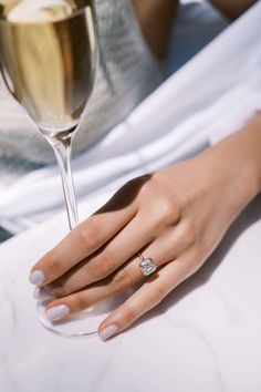 a woman's hand holding a wine glass with a diamond ring on the finger