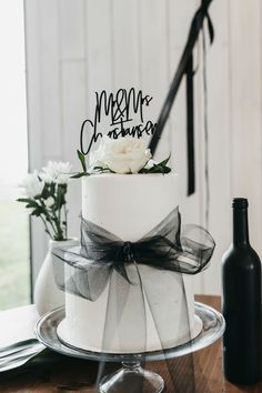 a white cake with a black bow on top and a wine bottle next to it