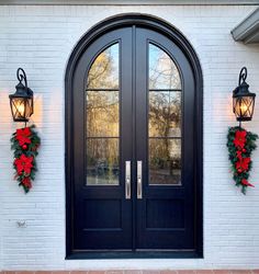 two christmas wreaths hanging on the side of a black double door with glass panels