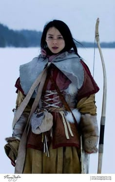 a woman dressed in native american clothing holding a bow and arrow while standing on snow covered ground