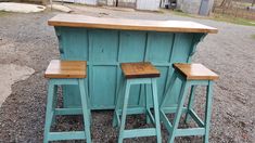 three wooden stools sitting next to each other on top of gravel covered ground in front of a barn