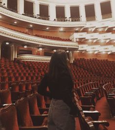 a woman standing in front of an auditorium filled with red seats and looking at the ceiling