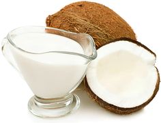 a glass bowl filled with coconut milk next to a cut in half coconut on a white background