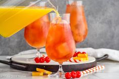 orange juice being poured into two glasses with candy canes on the side and in front