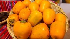 a basket filled with lots of yellow fruit on top of a colorful table cloth next to other fruits