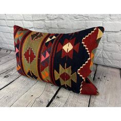 a colorful kilim pillow sitting on top of a wooden floor next to a brick wall