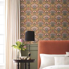 a bedroom with a bed, nightstand and lamp in front of a wallpapered wall