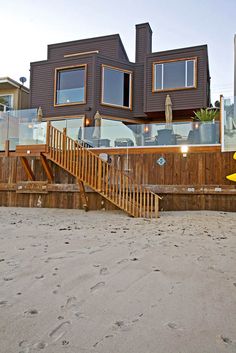 there is a surfboard on the beach next to a house that has stairs leading up to it