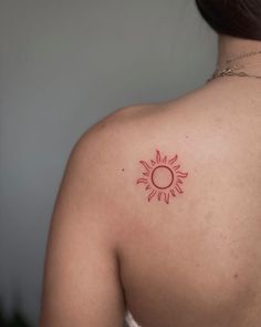 the back of a woman's shoulder with a small sun tattoo on her upper arm