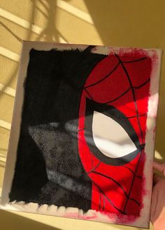 someone holding up a paper cut out of a spiderman mask