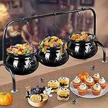 a table topped with black pots filled with halloween treats and cupcakes on top of it