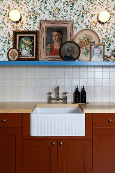 a kitchen sink under a shelf with pictures on the wall and above it is a painting