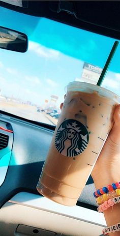 a woman holding up a cup of coffee in her hand while sitting in a car