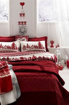 a bed with red and white comforters in a room next to two windows, decorated with christmas decorations