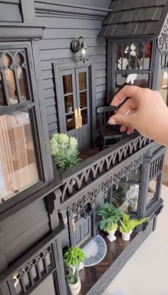 a hand is holding a black doll house with plants in the front and side windows