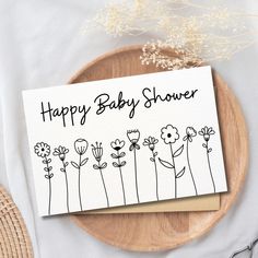 a happy baby shower card sitting on top of a wooden plate next to some flowers