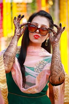 a woman with henna tattoos holding her hands up to her face and wearing sunglasses