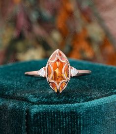 an orange and white diamond ring sitting on top of a green velvet covered tablecloth