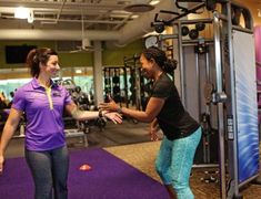 two women in a gym talking to each other while standing next to an exercise machine