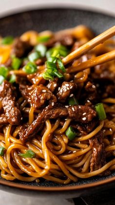 beef and noodles with chopsticks in a black bowl