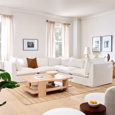 a living room filled with white furniture and lots of natural wood flooring in front of two windows