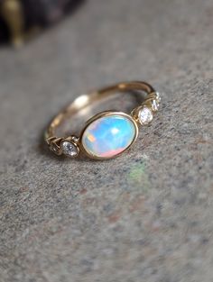 a white opal and diamond ring sitting on top of a gray stone surface,