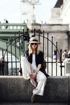 a woman sitting on top of a stone bench next to a black iron fence and wearing a hat